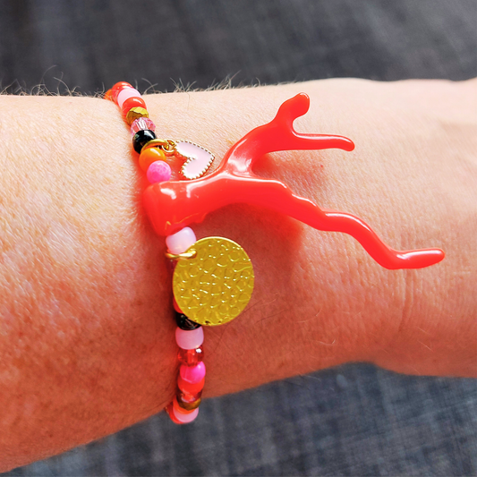 Armband in rode en roze rocailles met een rood koraal takje als eye-catcher. Sfeerfoto van armband om pols.