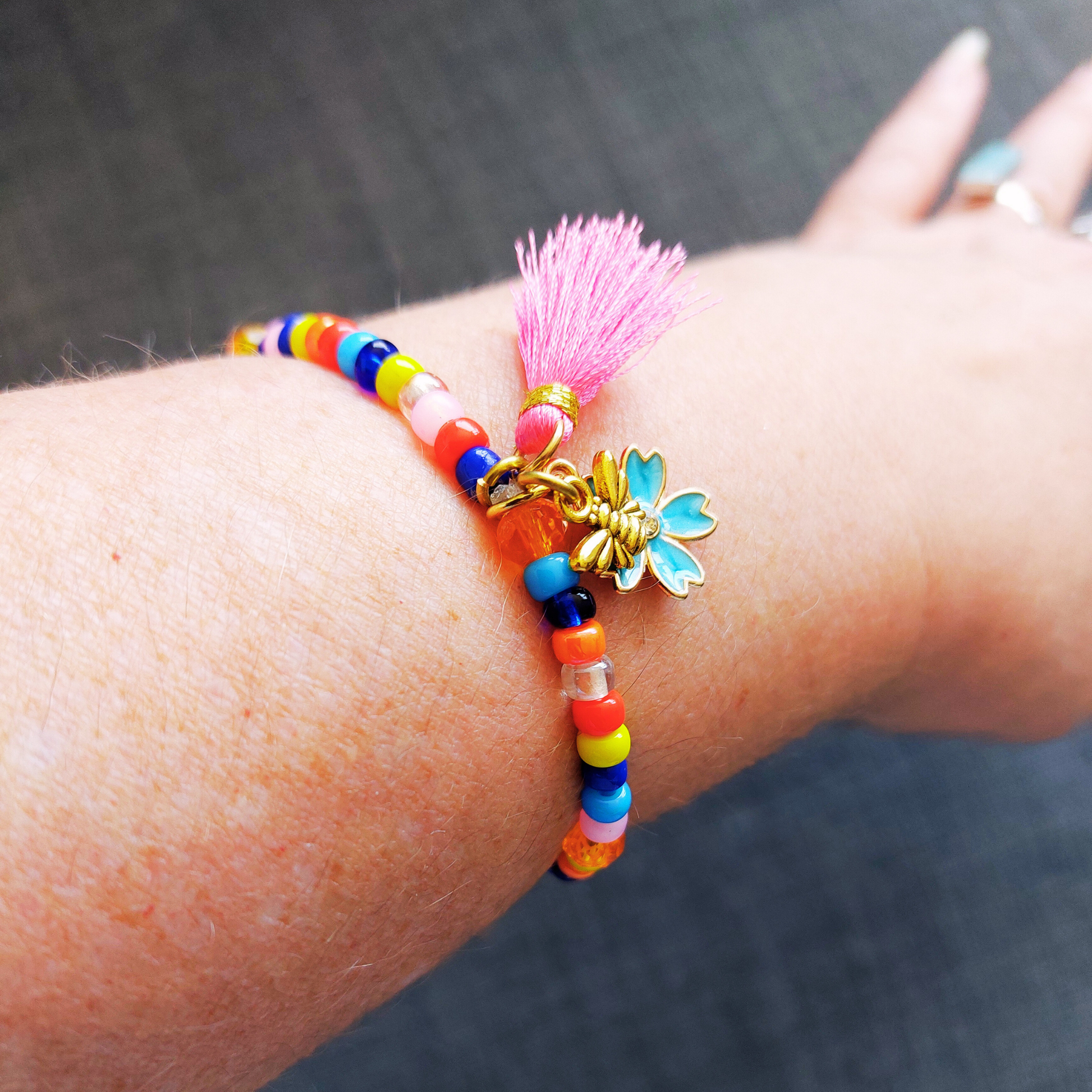 Armband met rocailles in diverse kleuren en met blauwe bloem bedel. Sfeerfoto van armband om pols.