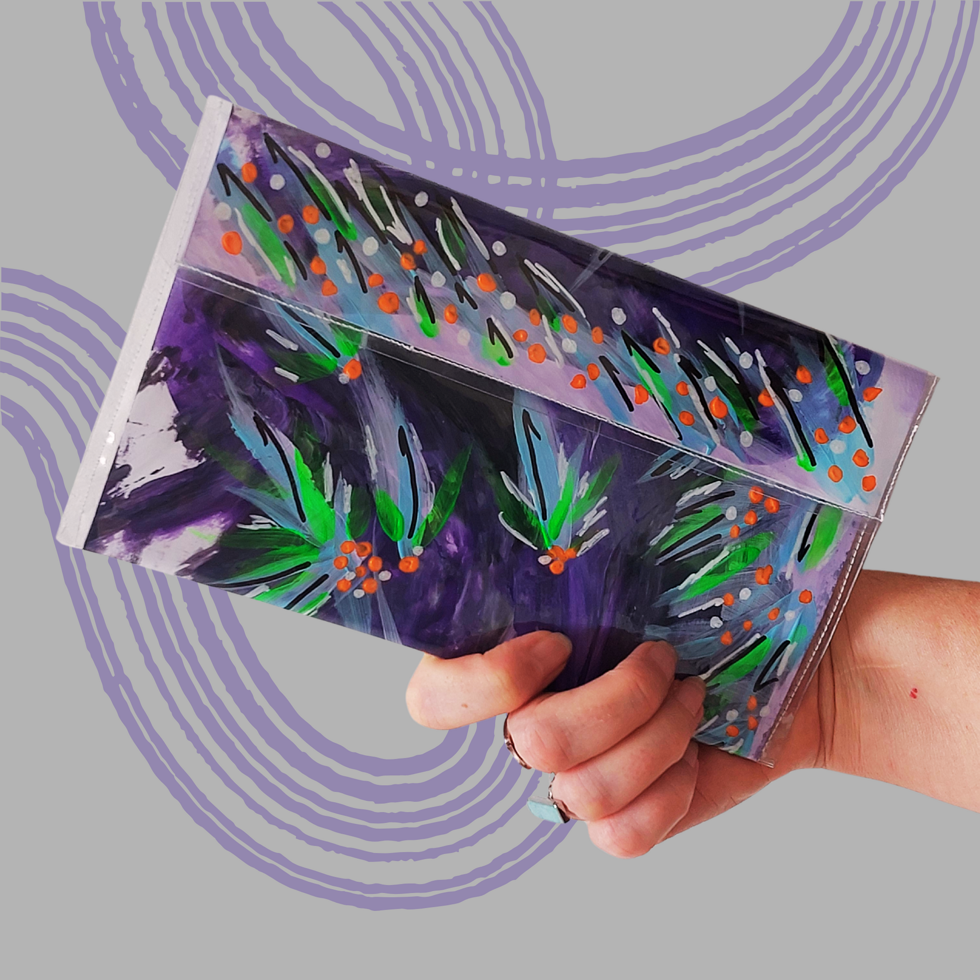 Tasje  in paars en lila met een bloempatroon in groen, oranje, zwart en wit accenten. Sfeerbeeld